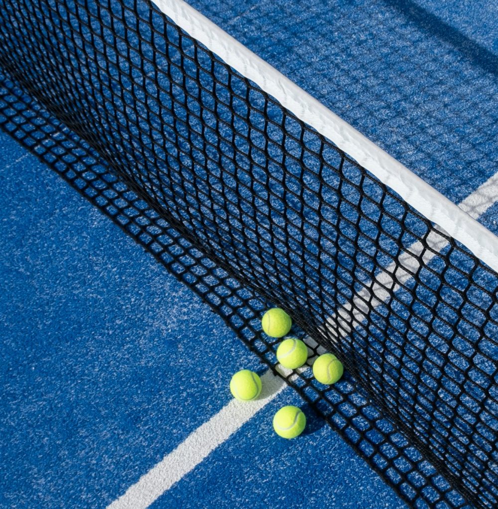 paddle tennis balls by the net on a blue paddle tennis court